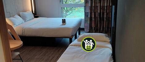 A hotel room with two beds, a small table, and a window with curtains.
