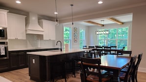 A modern kitchen with dark cabinetry, a central island, and a dining area with wooden tables and chairs.