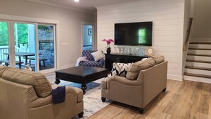 A spacious living room with a flat-screen TV, a fireplace, and a staircase.