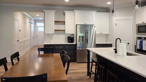 A modern kitchen with white cabinetry, a stainless steel refrigerator, and a wooden dining table.