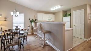 Une cuisine moderne avec des meubles blancs, un îlot central doté de tabourets, une table à manger avec des chaises et un luminaire suspendu.