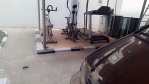 A gym with exercise equipment, a car, and a white wall. - Zek Dynasty (Lagos)