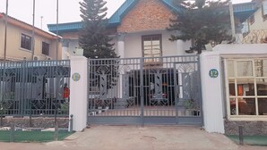 A gated entrance with a number 12 sign, a white building with a blue roof, and a small balcony. - Zek Dynasty (Lagos)