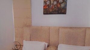 A bedroom with a bed, two pillows, a nightstand with a lamp, and a wall-mounted painting. - Zek Dynasty (Lagos)