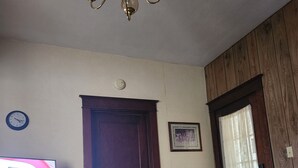 Un soggiorno con una porta in legno, una sveglia, un quadro incorniciato, un televisore e un cestino.