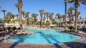 Une grande piscine extérieure entourée de palmiers et de chaises longues.