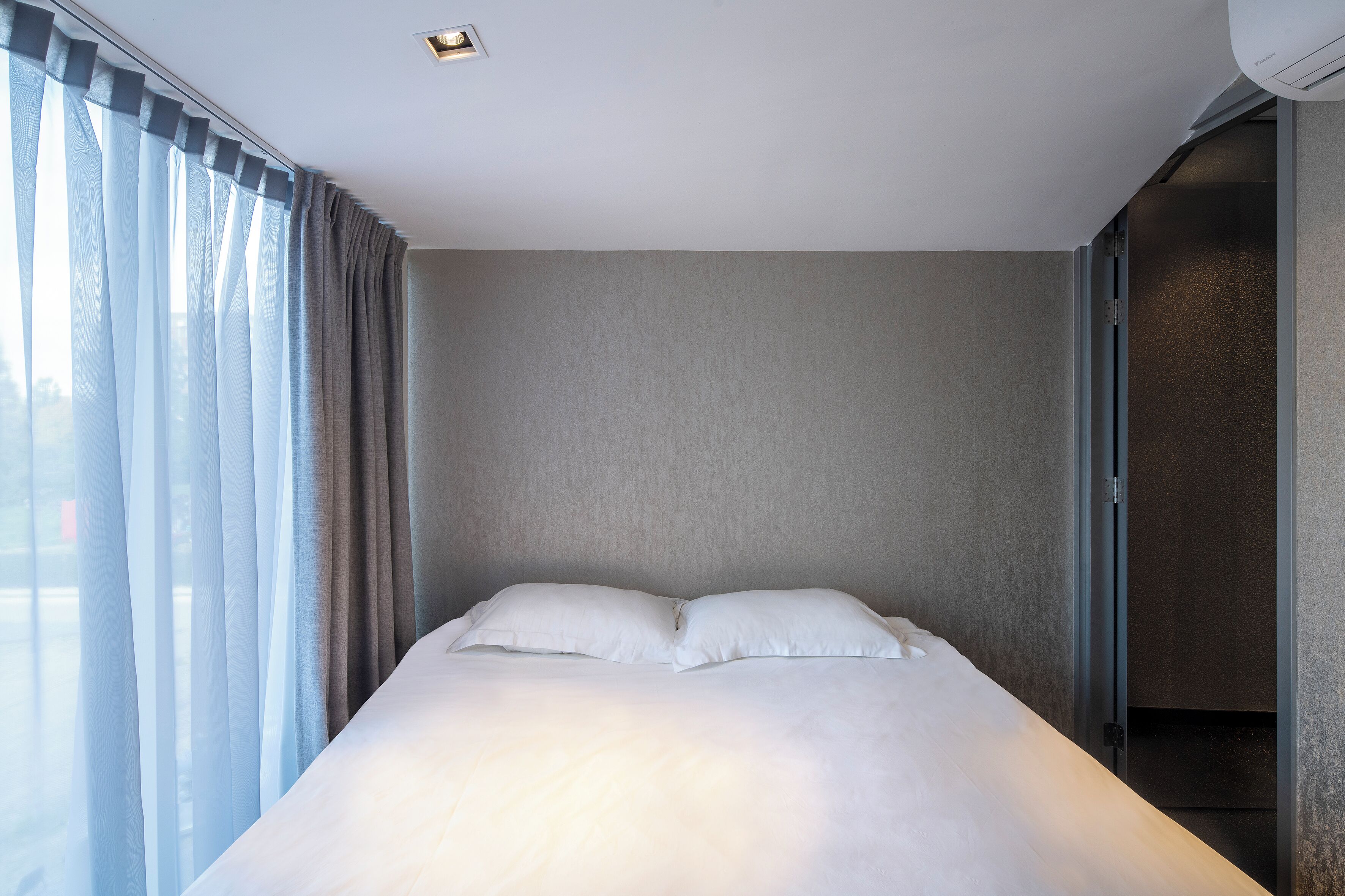 A modern hotel room with a large bed, sheer curtains, and a view through the window.