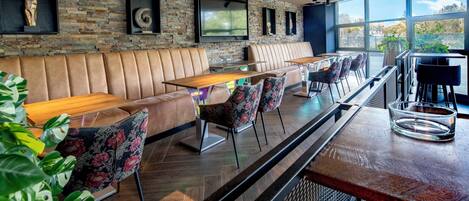 Un área de bar moderna con asientos de cuero, un televisor grande y vistas al exterior.