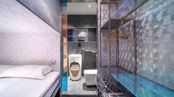 A compact hotel room with a bed, a small bathroom with a toilet and sink, and a shower area.