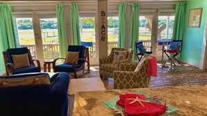 Ein Zimmer mit einer Sitzecke, ausgestattet mit zwei blauen Sesseln, einem gemusterten Sofa und einem kleinen Tisch mit roten Servietten und Meeresstern-Dekorationen.