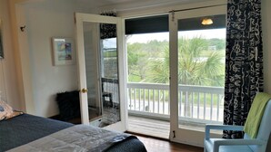 Ein Schlafzimmer mit Bett, Stuhl, einem Balkon mit Blick auf Grünflächen und einer Tür mit Glasfenster.