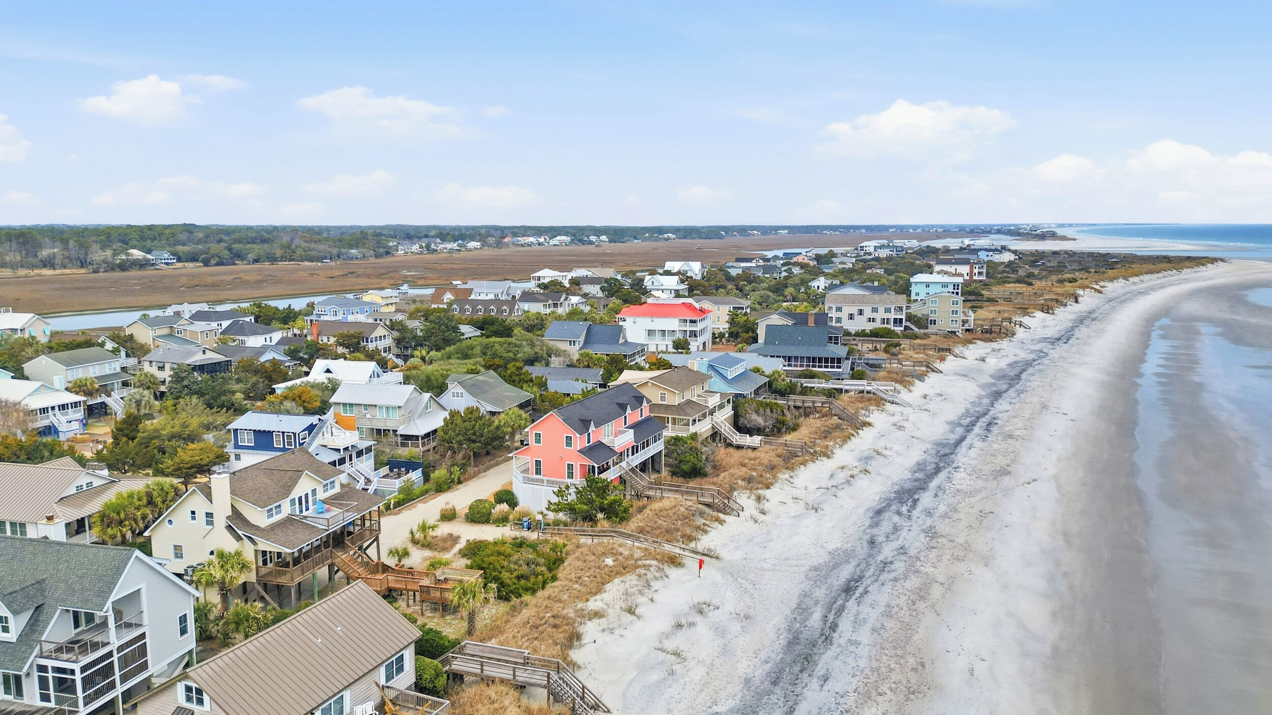 A coastal residential area with houses along the beach, featuring a mix of single and multi-story buildings, some with decks and others with attached garages.