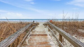 A wooden boardwalk leading to a beach with sand and sparse vegetation. - Arrogantly Shabby - Oceanfront (Pawleys Island)