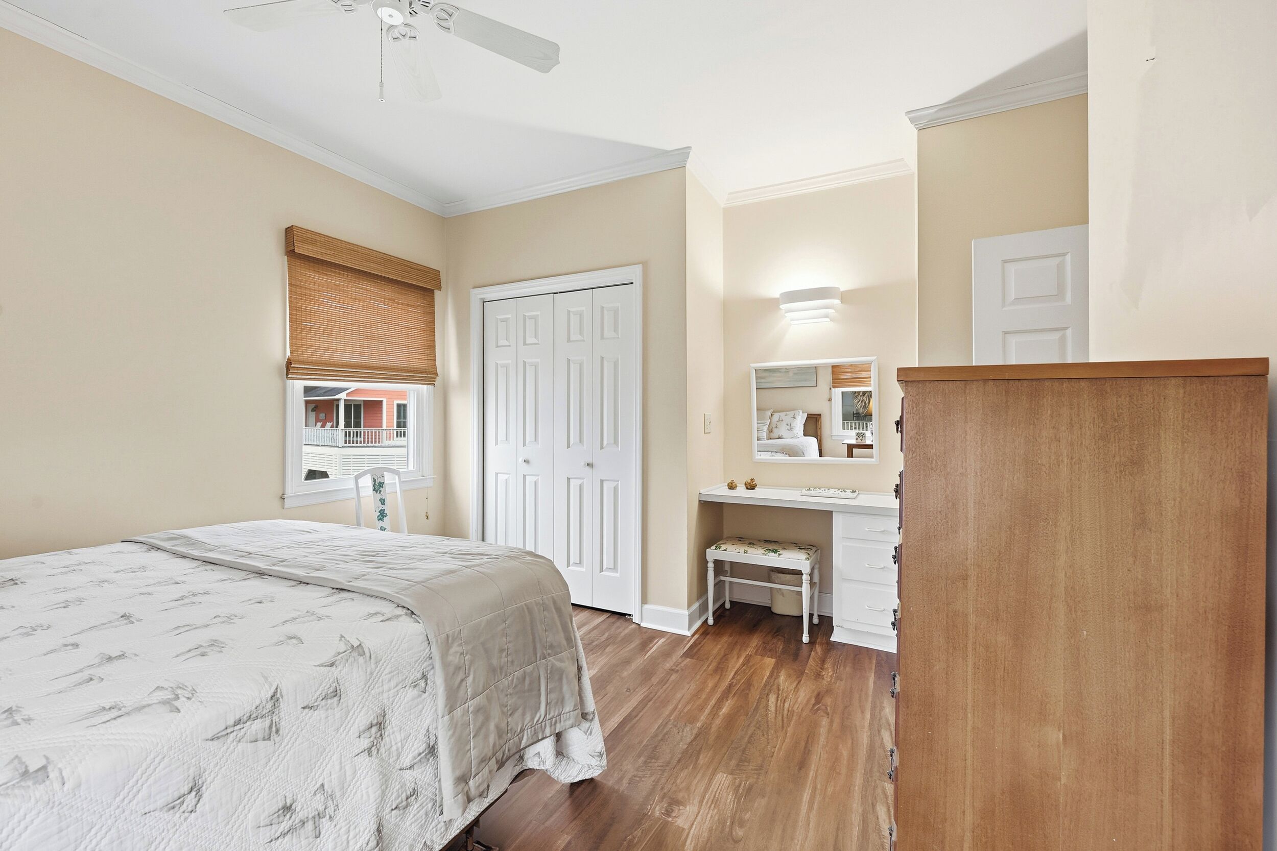 A bedroom with a bed, a vanity with a mirror, a door, and a ceiling fan.