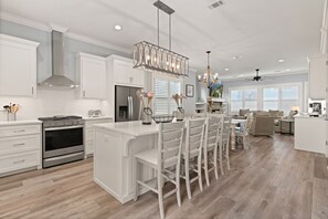 A modern kitchen with white cabinetry, a central island with bar stools, stainless steel appliances, and pendant lighting.