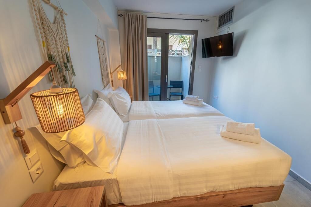 A hotel room with two beds, a TV mounted on the wall, a lamp, and a view of an outdoor balcony.