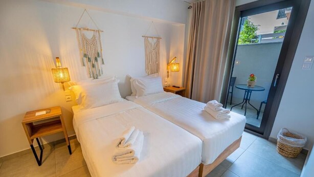 A hotel room with two beds, a small table, and a balcony with a table and chairs. - Niso Skiathos (Skiathos)