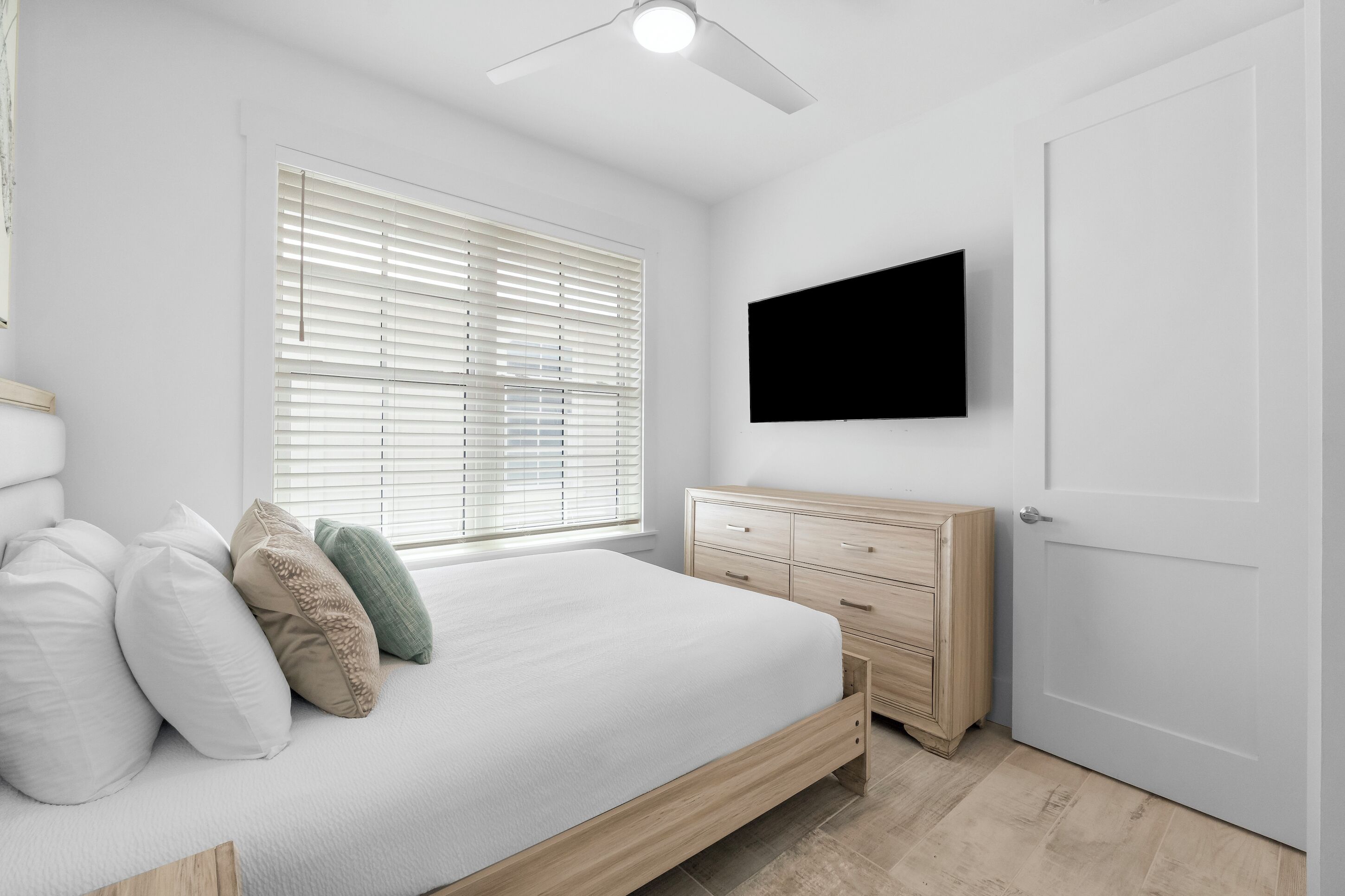 Een slaapkamer met een bed, een houten dressoir, een aan de muur bevestigde televisie en een raam met zonwering.