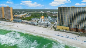 An aerial view of a coastal hotel with multiple buildings, a beach, and ocean waves. - Beach House - Reel Em Inn by PHG (Panama City Beach)