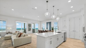 A spacious living area with a large island, a dining set, and a view of the ocean. - Beach House - Reel Em Inn by PHG (Panama City Beach)
