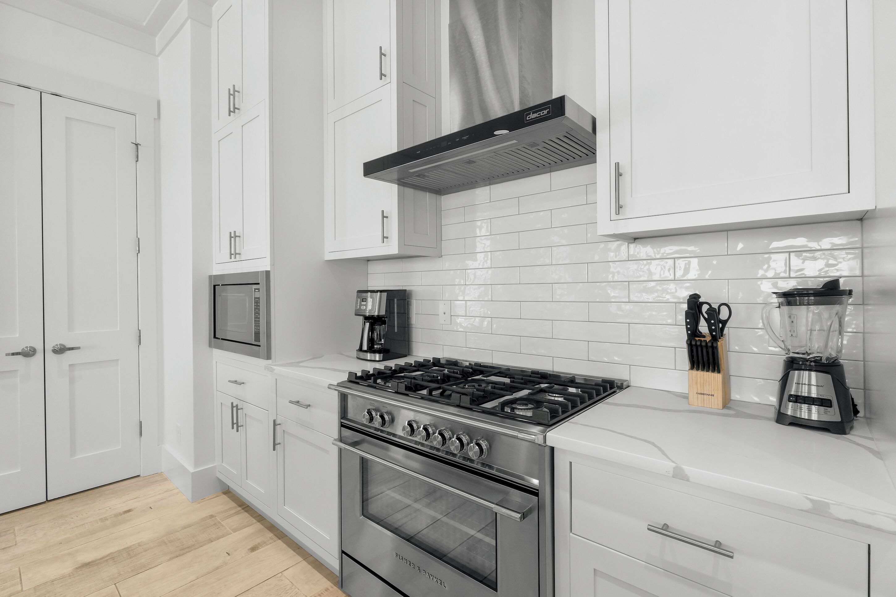A modern kitchen with white cabinets, a stainless steel stove, a microwave, and a coffee maker.