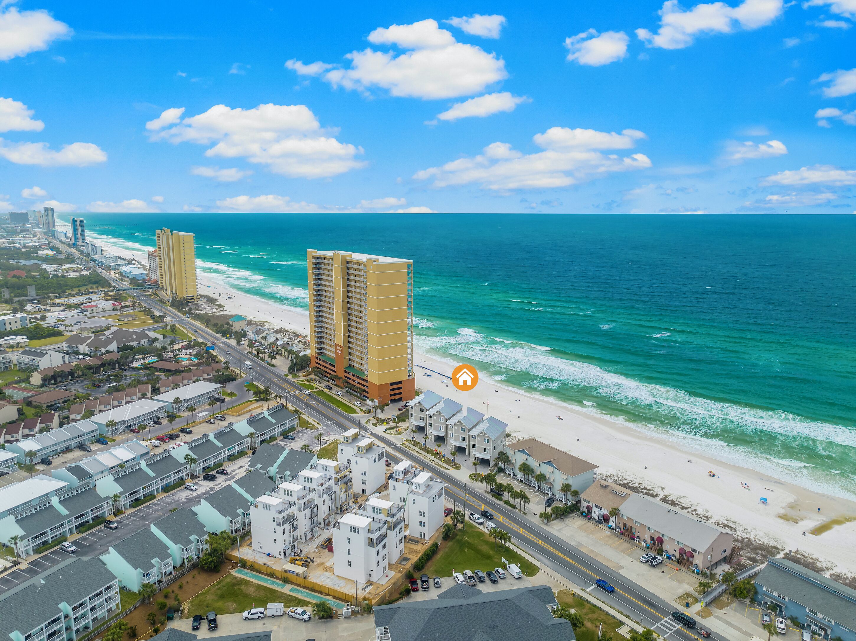 A coastal cityscape with a beachfront hotel, a road, and residential buildings.