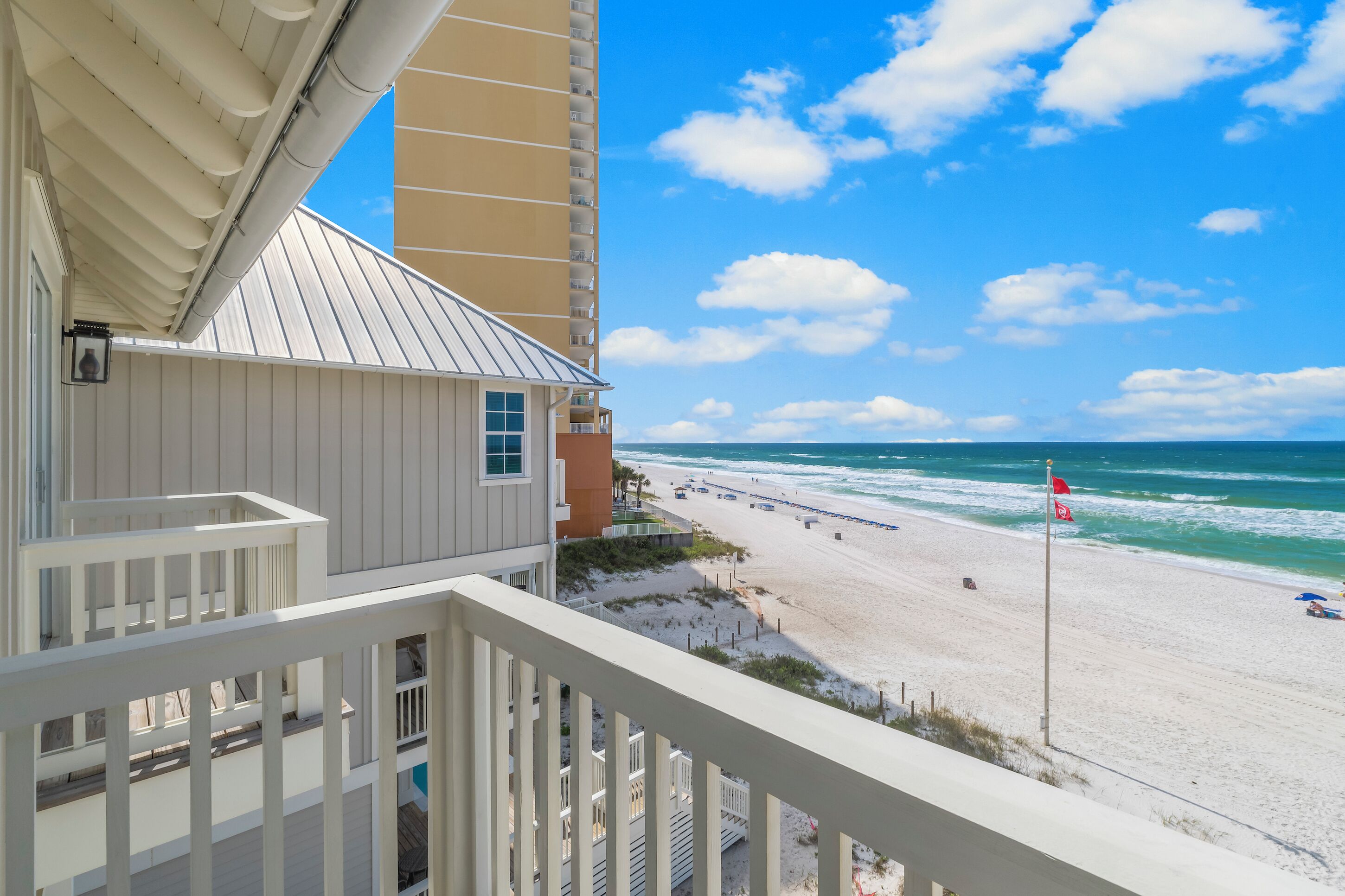 A beachfront property with a balcony overlooking the ocean, a sandy beach, and a clear sky.