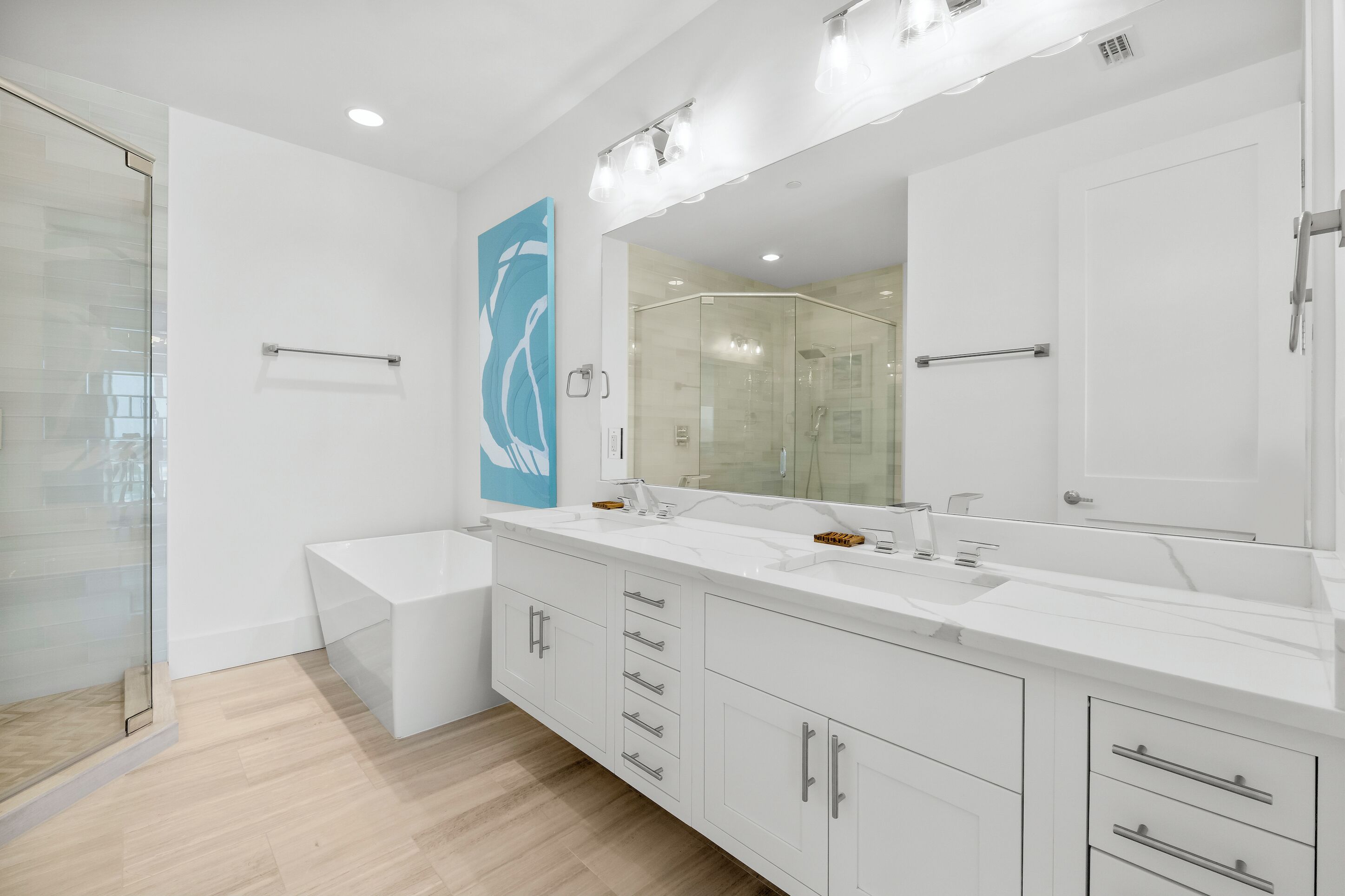 A modern bathroom with a glass shower enclosure, a large mirror, and a white vanity with multiple drawers.