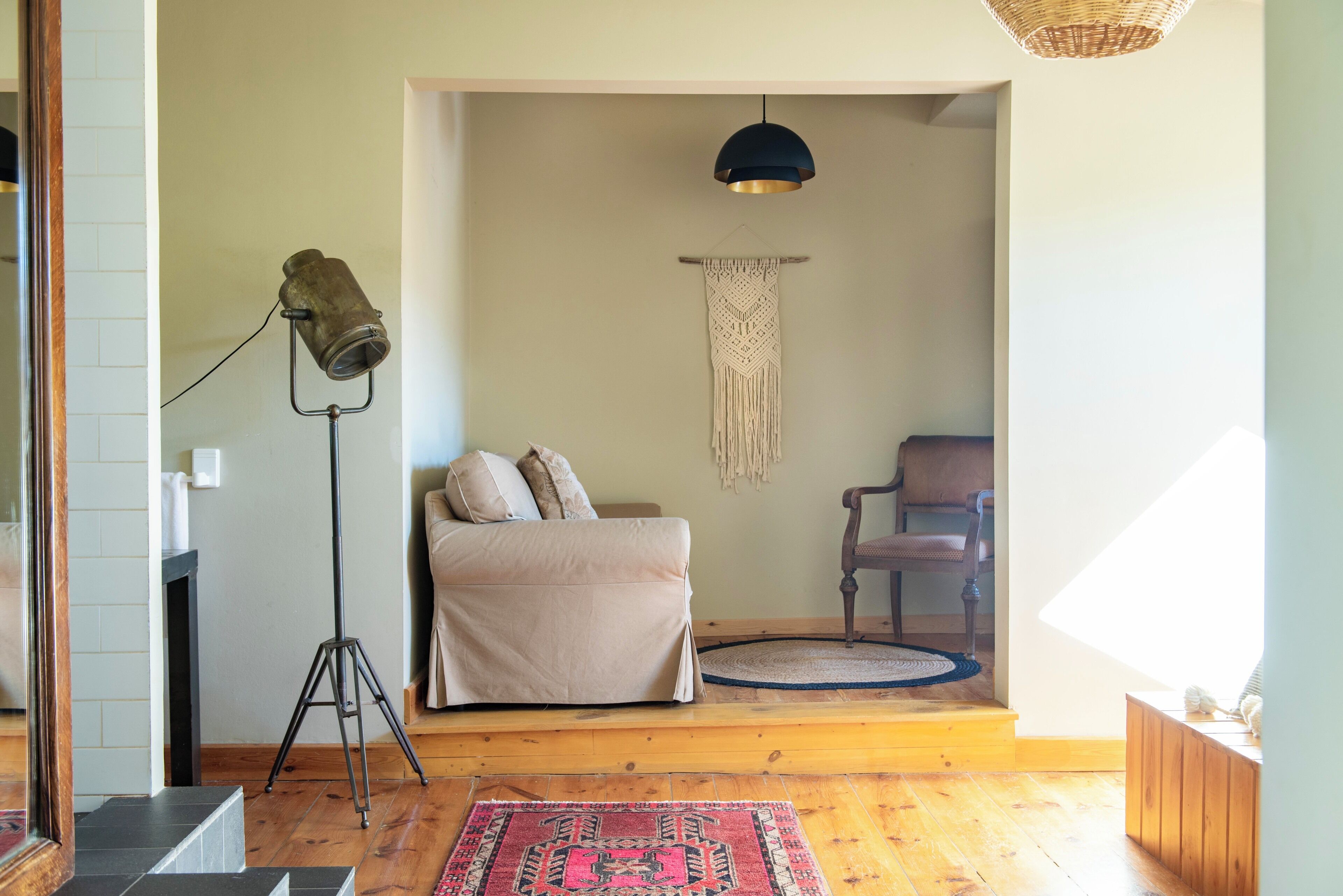 Una habitación acogedora con cama, lámpara de pie, tapiz de macramé y una lámpara de techo de mimbre.