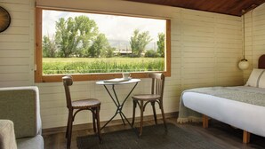 A room with a bed, two chairs, a small table, and a window with a view of a field and trees. - Mas Sant Marc (Puigcerda)