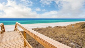 Een houten looppad dat naar een strand leidt met helder turquoise water en een gedeeltelijk bewolkte lucht.