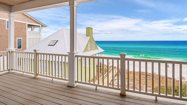Een houten terras met een witte balustrade, uitkijkend op een strand en de oceaan.