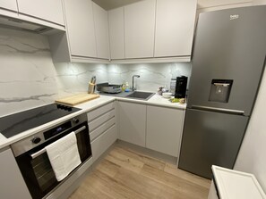 A modern kitchen with white cabinets, a stainless steel refrigerator, a black stove, and a wooden countertop. - Luxury Apartment in Letchworth (Letchworth Garden City)