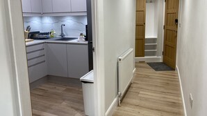Un pasillo estrecho que conduce a una cocina con armarios blancos, un lavabo y un radiador.