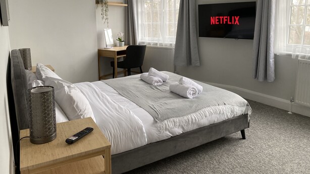 Habitación de hotel con cama, escritorio, silla, televisor montado en la pared y ventana con cortinas.