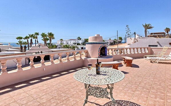 A rooftop terrace with a round table, lounge chairs, and a decorative wall.