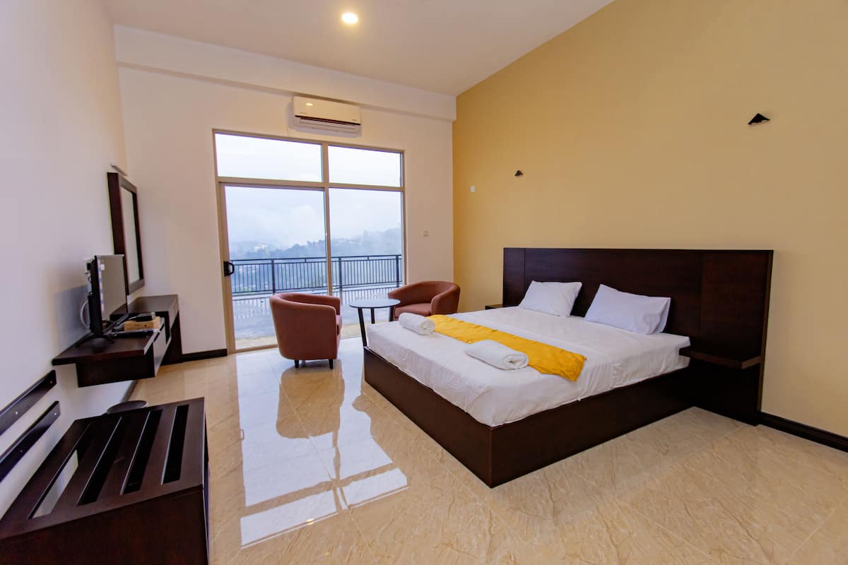 A hotel room with a large bed, a desk with a computer, a chair, and a view of the outdoors through a large window.