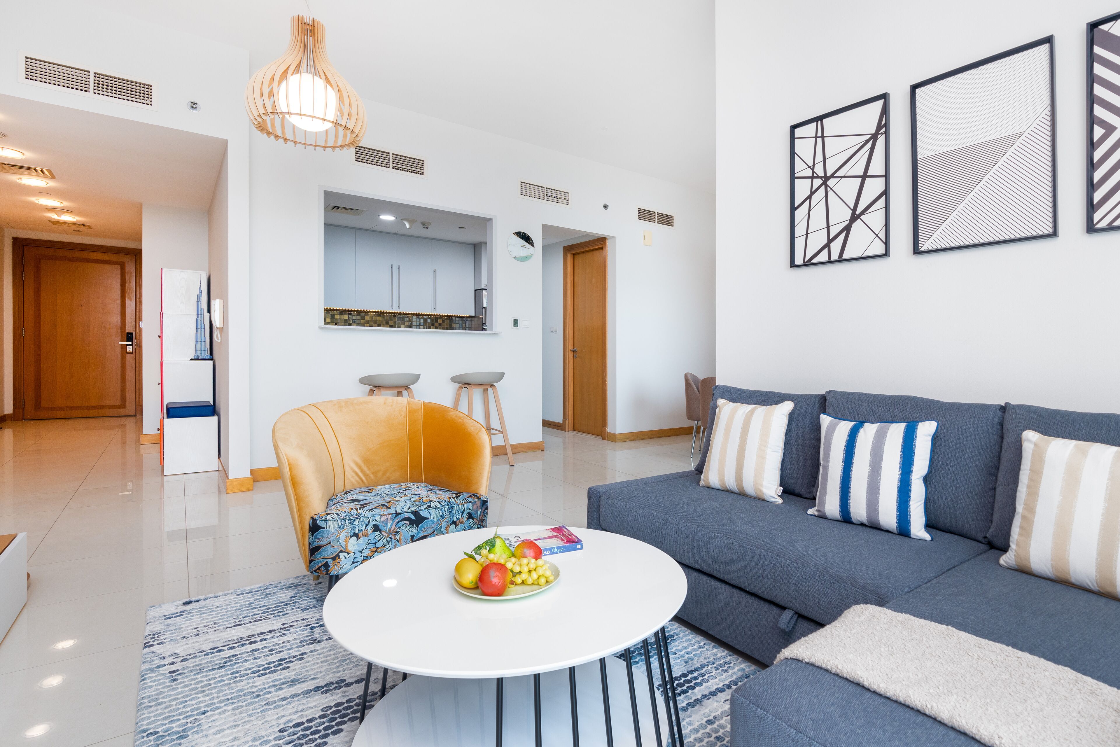 A modern living room with a sofa, a coffee table with fruit, and a kitchen in the background.