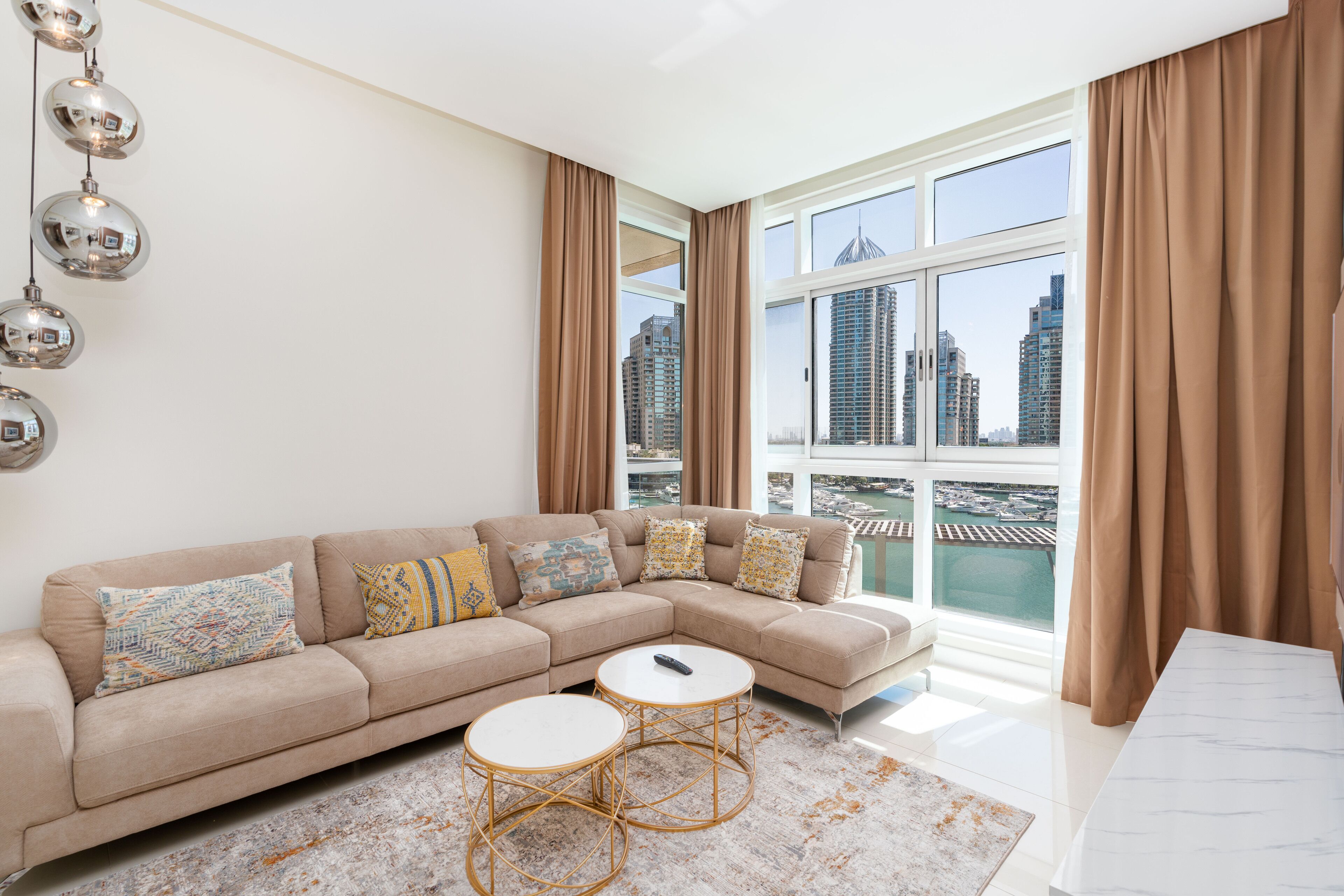 A modern living room with a beige sectional sofa, two round coffee tables, and a large window with a view of a cityscape and water.