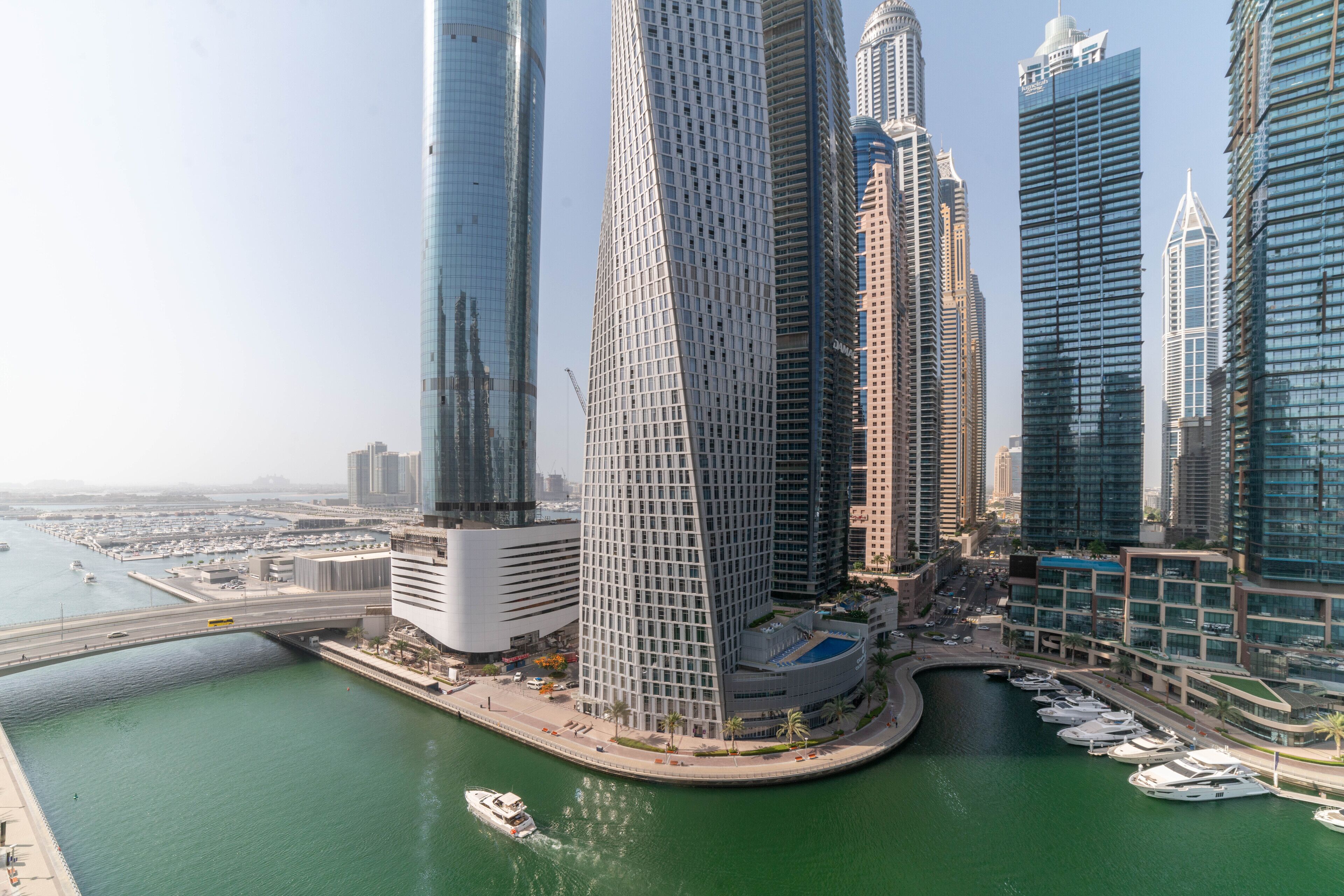 A high-rise urban area with modern skyscrapers, a marina with boats, and a bridge connecting to the mainland.