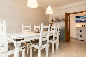 Ein Essbereich mit einem weißen Tisch und Stühlen, Pendelleuchten, einer Holztür und einem Gemälde an der Wand.