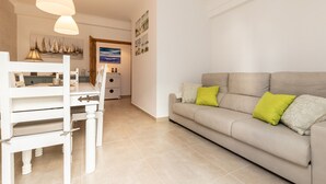 Una sala moderna con un sofá color beige, una mesa de comedor blanca y sillas. Hay dos lámparas colgantes sobre la mesa.