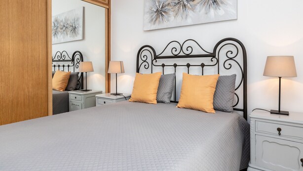 Un dormitorio ordenado con una cama, dos mesitas de noche y un tocador.
