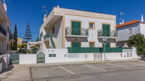 Un edificio de dos pisos con fachada blanca, contraventanas verdes y un balcón con barandilla de metal.