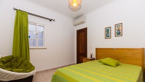 Una camera da letto con un letto, una poltrona verde, una porta in legno e due quadri appesi al muro.