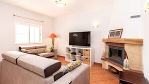 Een woonkamer met een bank, televisie, open haard en raam.