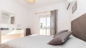 Een slaapkamer met een bed, nachtkastje, spiegel en een raam met gordijnen.