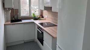 A modern kitchen with white cabinets, a black countertop, and a window with a view of buildings. - T2 Cozy à 20min du Stade de France (Saint-Denis)