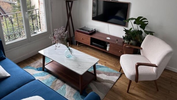 A living room with a sofa, coffee table, TV, and a plant. - T2 Cozy à 20min du Stade de France (Saint-Denis)