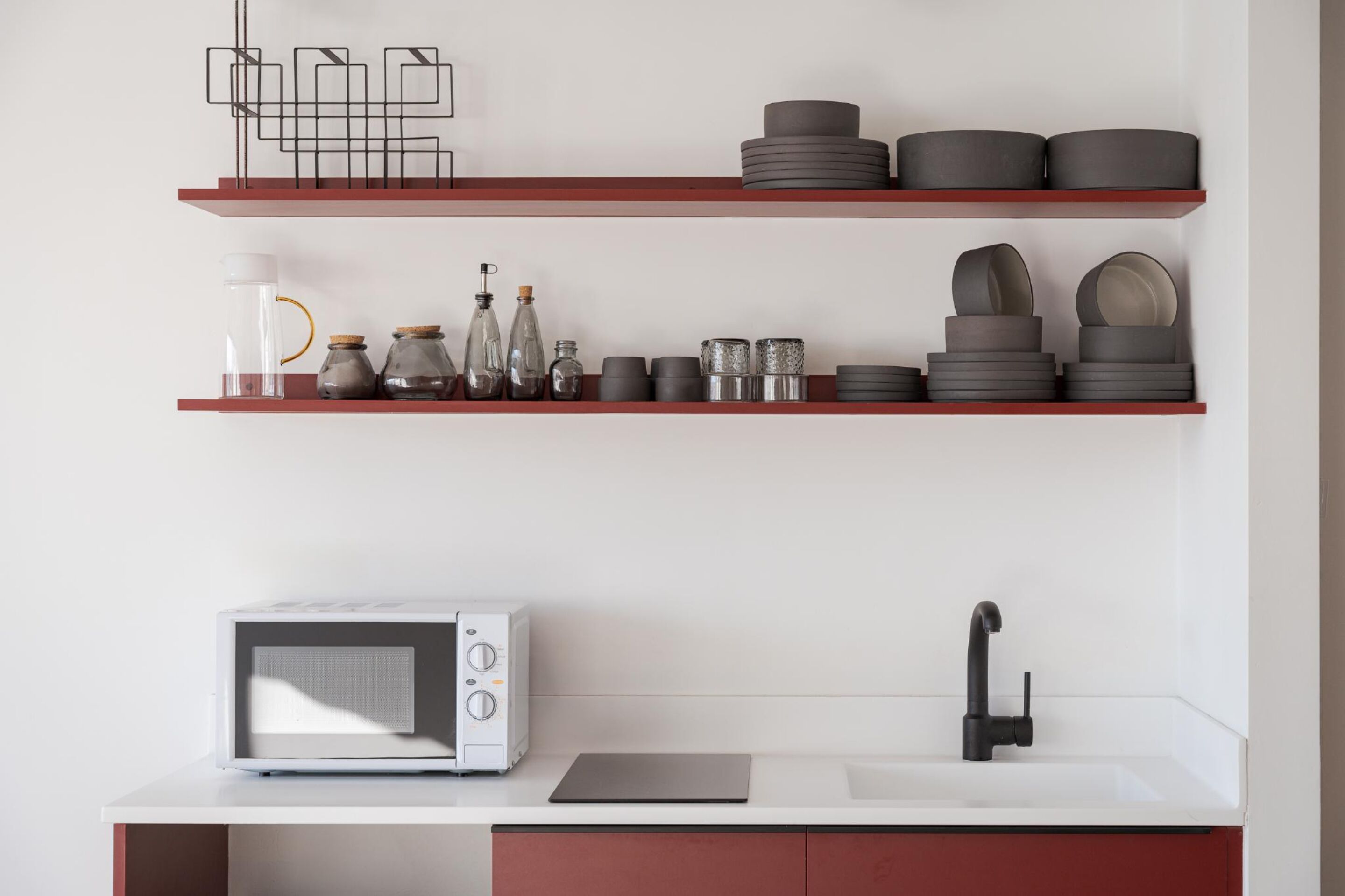 Une cuisine avec un micro-ondes blanc, un robinet noir et des étagères remplies d’ustensiles de cuisine.